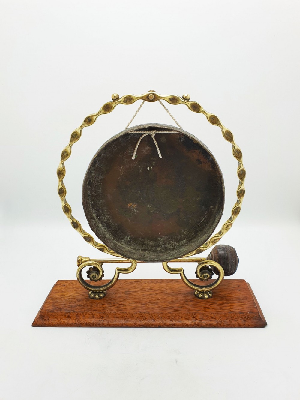 An antique brass circular gong with patterned etching suspended within a wavy brass frame on a polished rectangular oak base with a matching striker. View VII