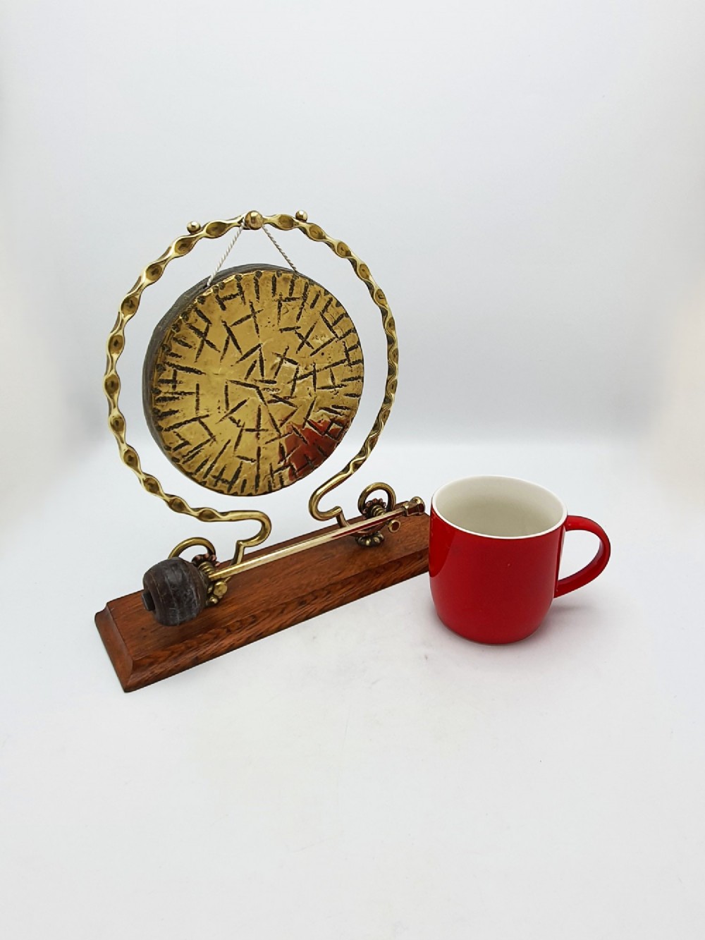 An antique brass circular gong with patterned etching suspended within a wavy brass frame on a polished rectangular oak base with a matching striker. View X