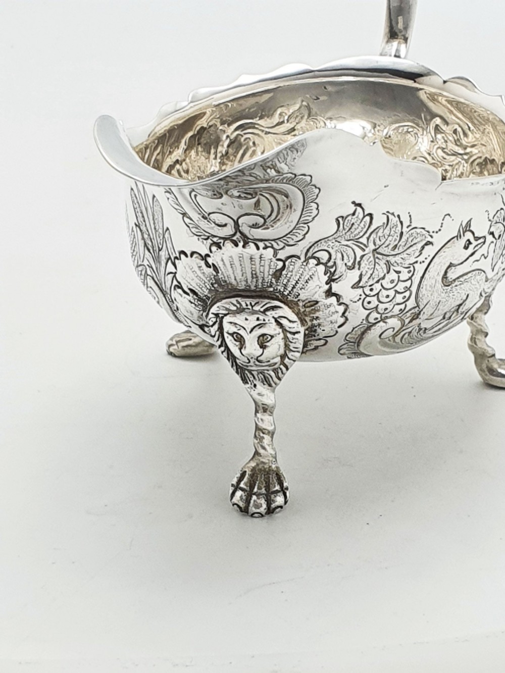 A pair of engraved silver-plated sauce boats with curved handles and decorated cabriole legs resting on a neutral background. View II