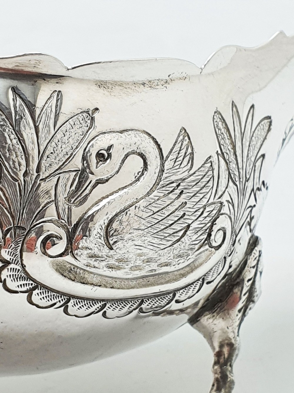 A pair of engraved silver-plated sauce boats with curved handles and decorated cabriole legs resting on a neutral background. View III