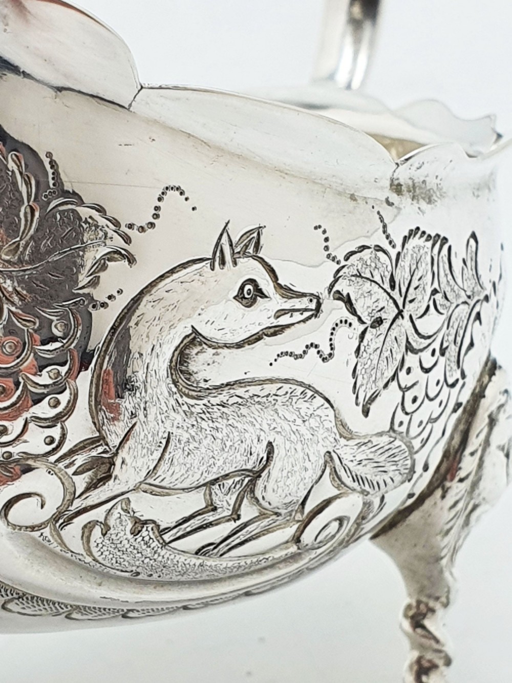 A pair of engraved silver-plated sauce boats with curved handles and decorated cabriole legs resting on a neutral background. View IV