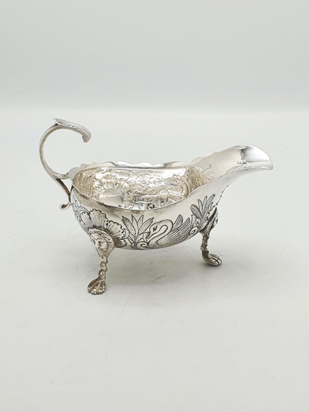 A pair of engraved silver-plated sauce boats with curved handles and decorated cabriole legs resting on a neutral background. View V