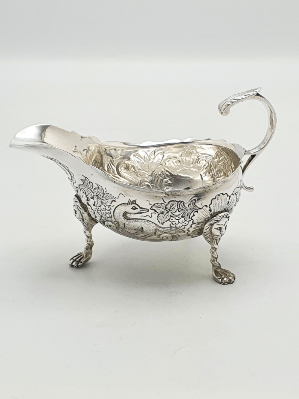 A pair of engraved silver-plated sauce boats with curved handles and decorated cabriole legs resting on a neutral background. View VI