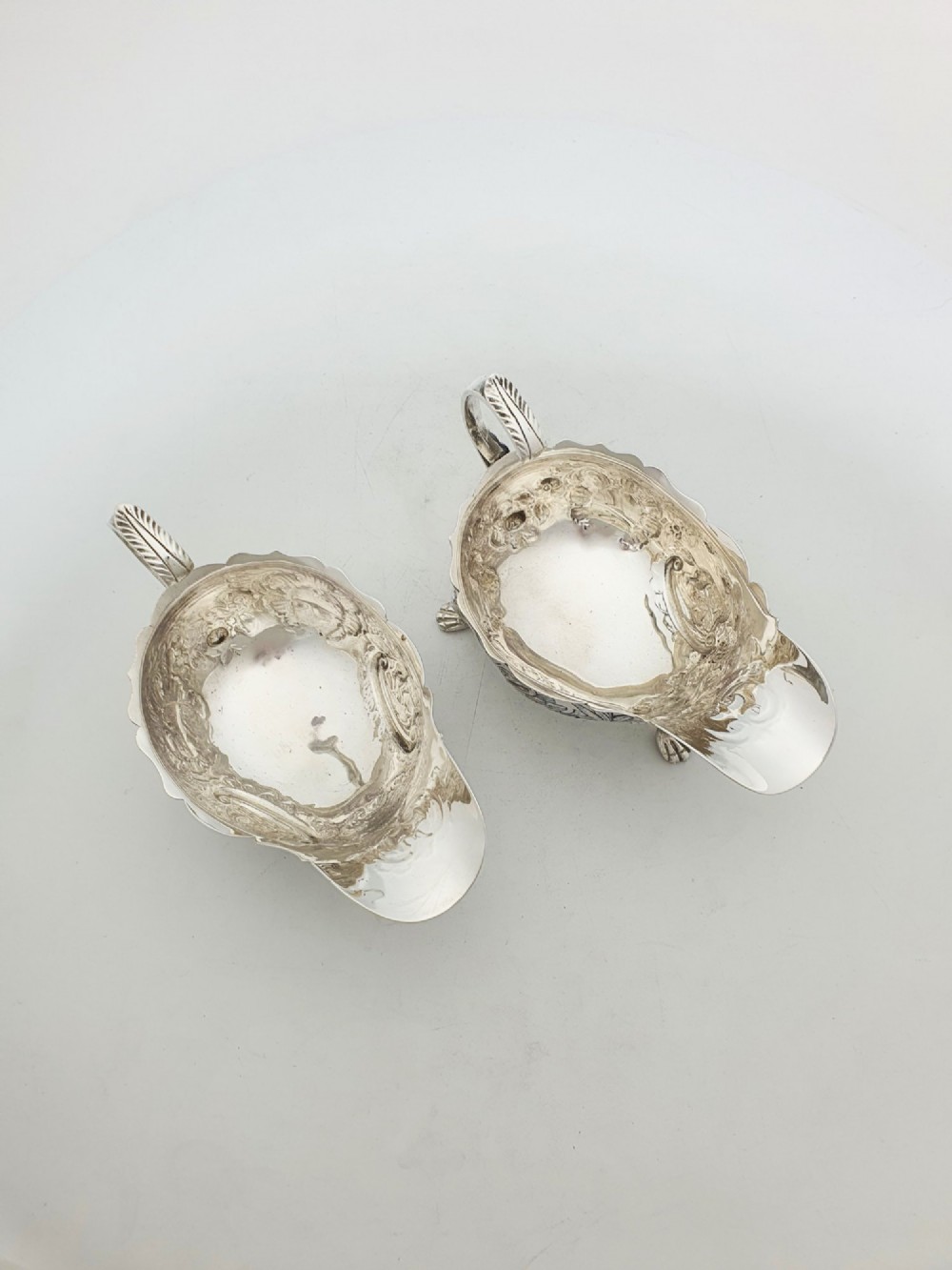 A pair of engraved silver-plated sauce boats with curved handles and decorated cabriole legs resting on a neutral background. View VIII