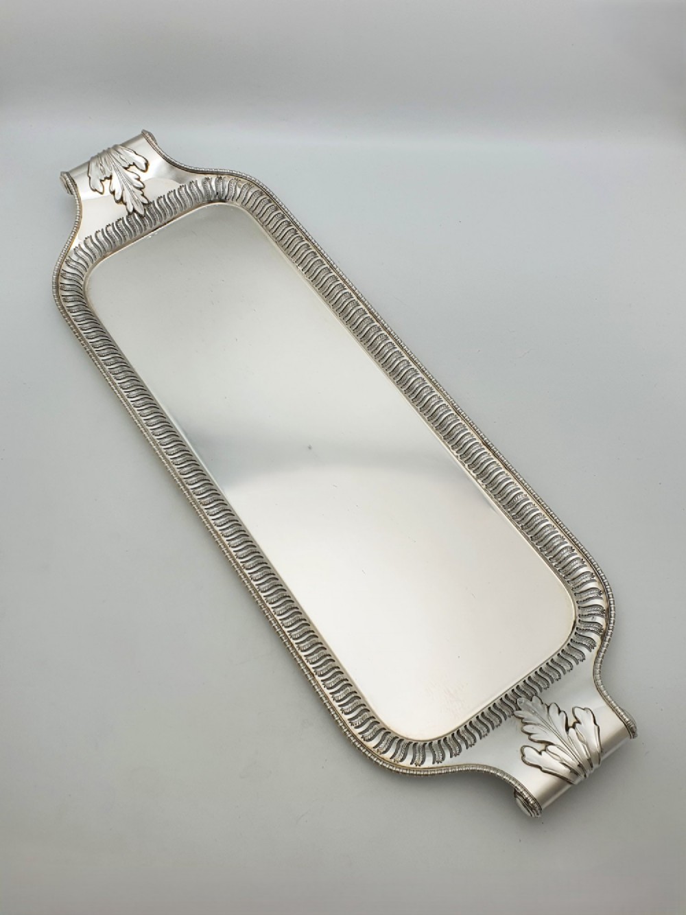An elongated rectangular silver-plated serving tray featuring a pierced wavy border and leaf-motif end handles.