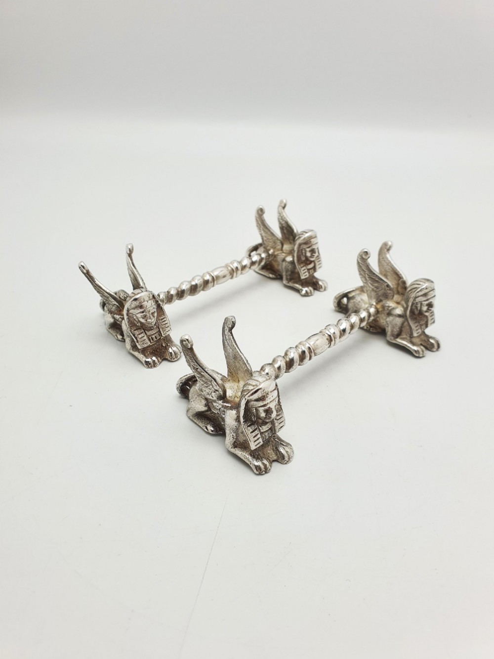 A pair of Victorian silver-plated knife rests featuring winged sphinx end supports connected by a spiral twist bar.