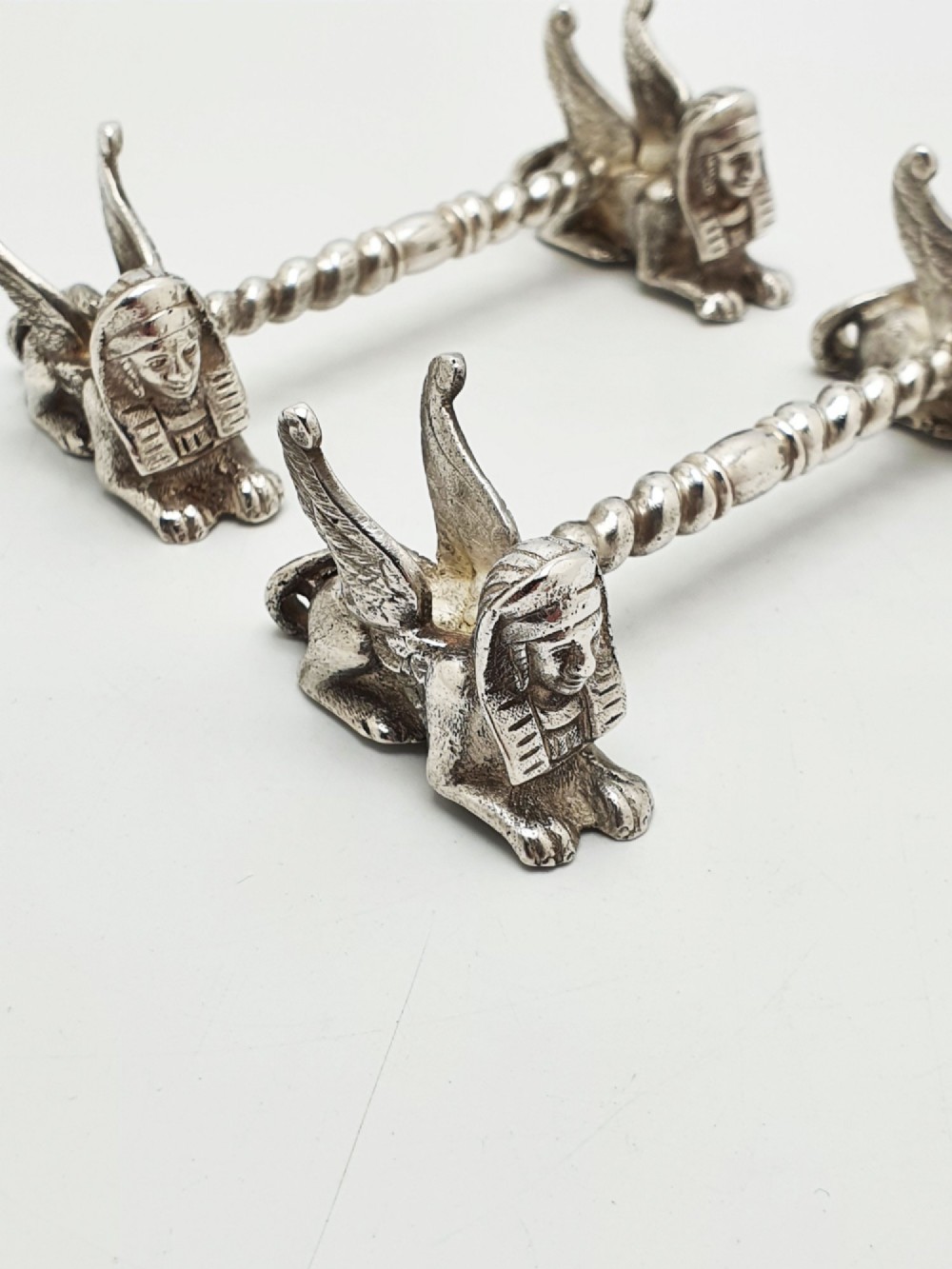 A pair of Victorian silver-plated knife rests featuring winged sphinx end supports connected by a spiral twist bar. View II