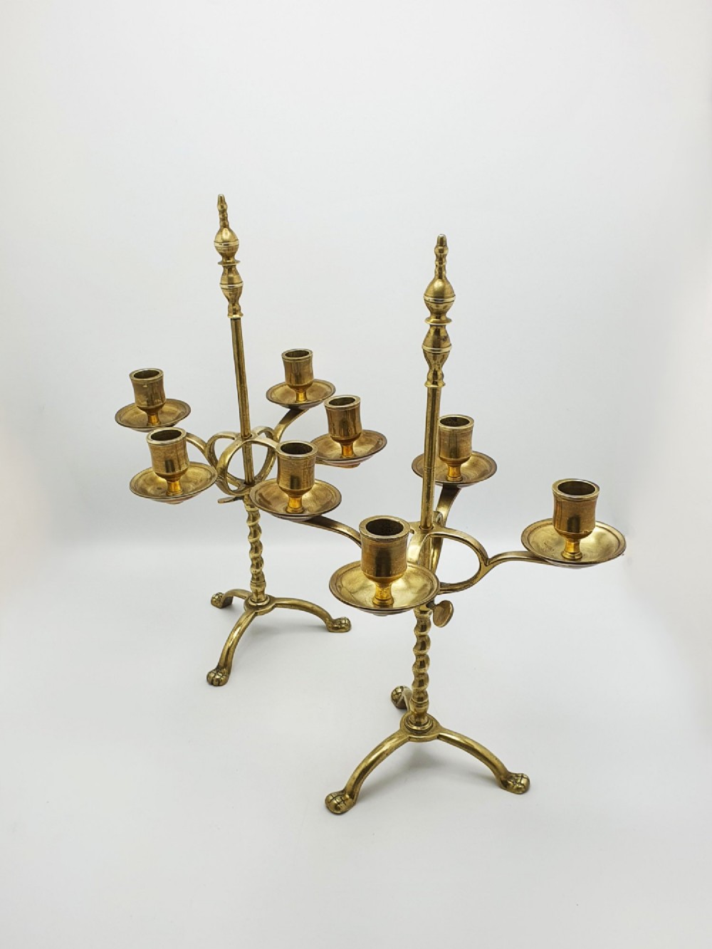 A pair of antique brass four-light adjustable candelabras featuring turned central shafts, tripod feet, and finials.