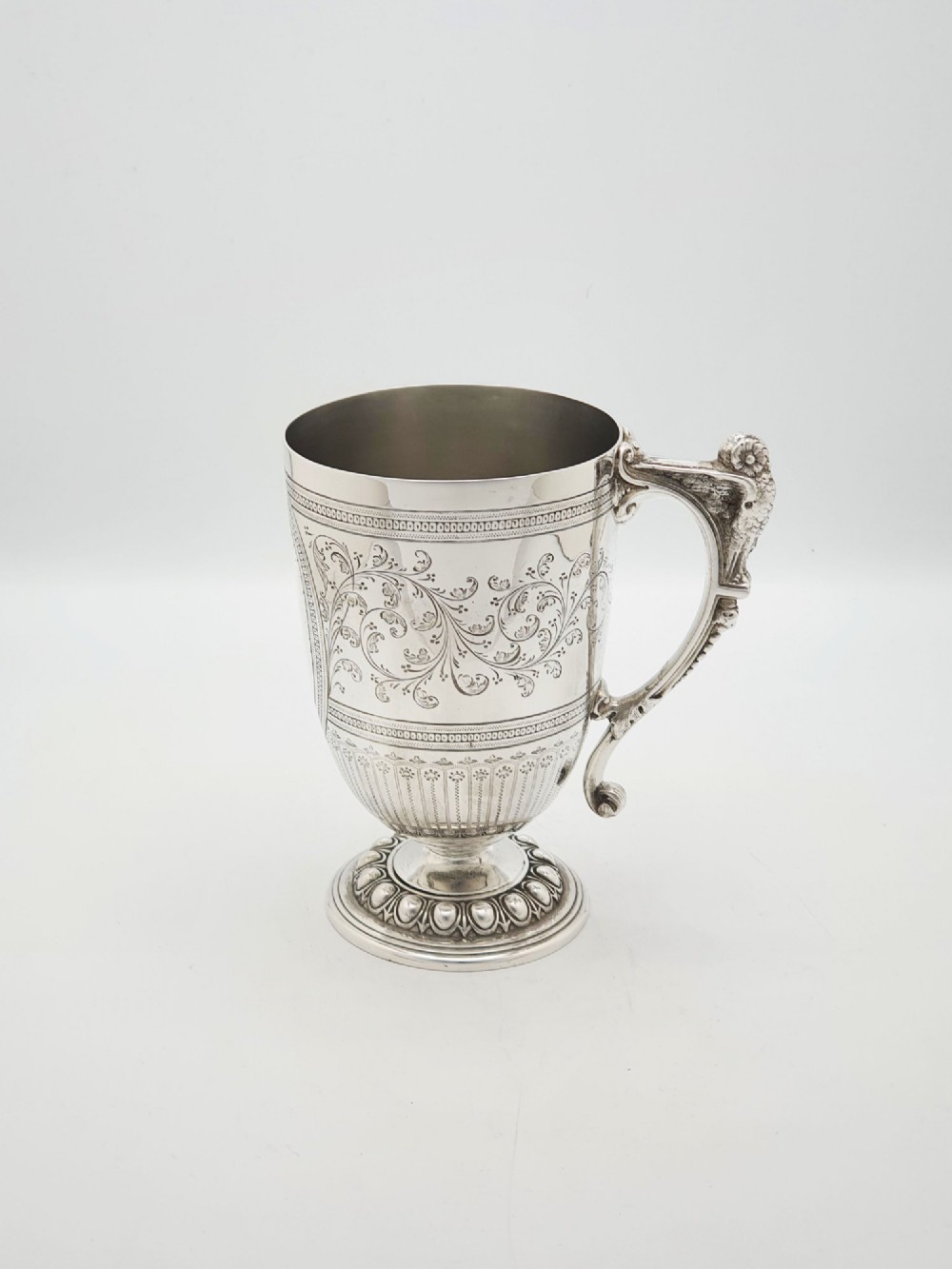 An Edwardian silver-plated tankard with intricate foliate engraving, a fluted pedestal base, and a decorative handle sculpted with an owl motif.