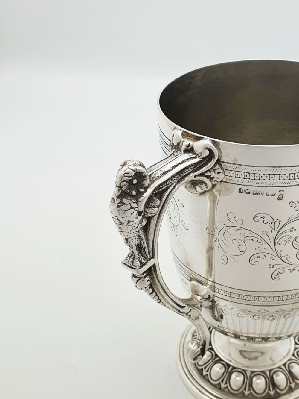 An Edwardian silver-plated tankard with intricate foliate engraving, a fluted pedestal base, and a decorative handle sculpted with an owl motif. View V
