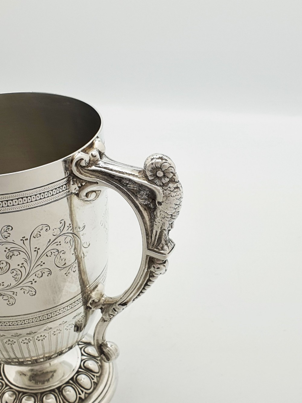 An Edwardian silver-plated tankard with intricate foliate engraving, a fluted pedestal base, and a decorative handle sculpted with an owl motif. View VI