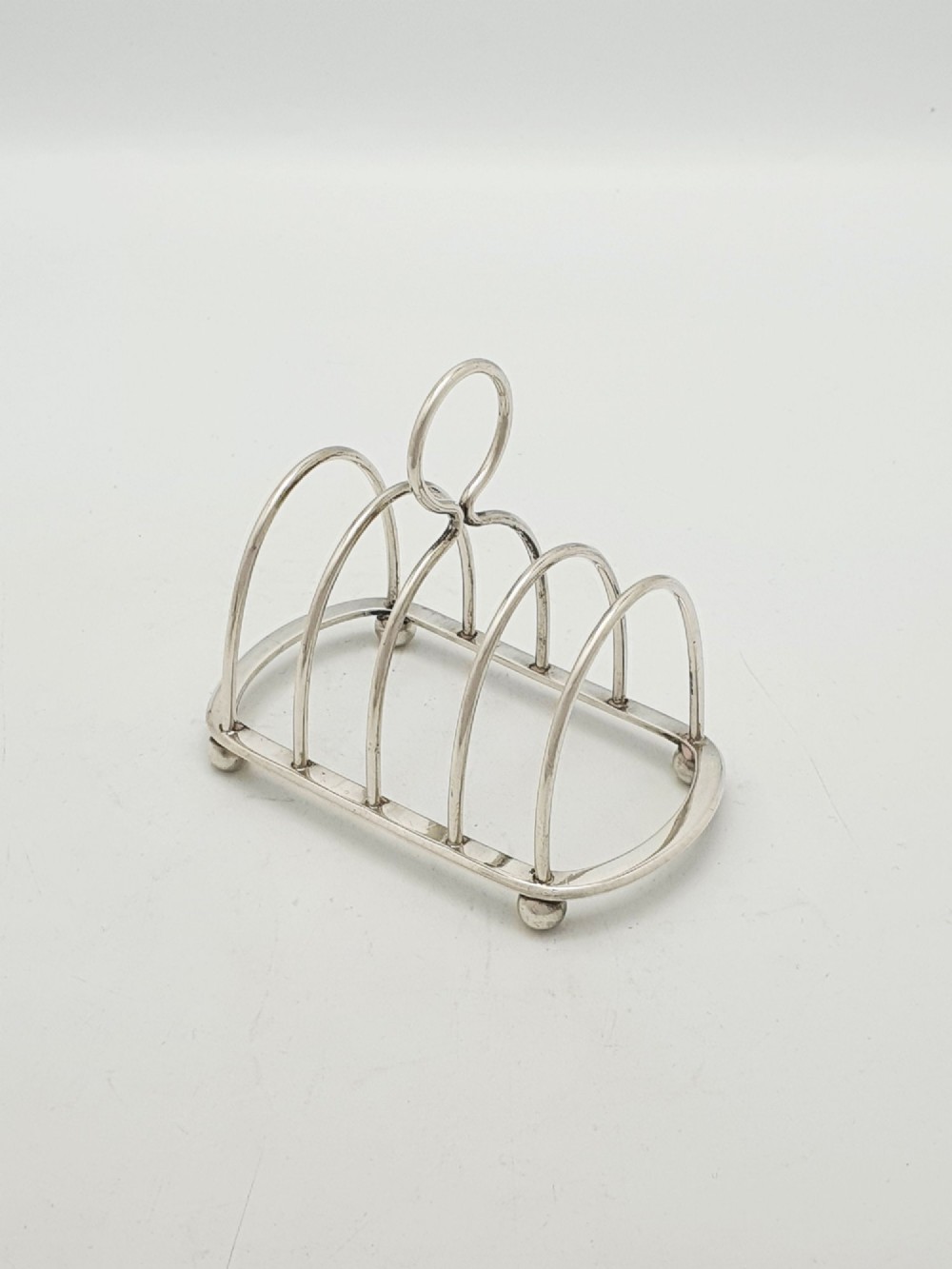 A small late Victorian sterling silver toast rack featuring five arched divisions, a central ring handle, and four ball feet.