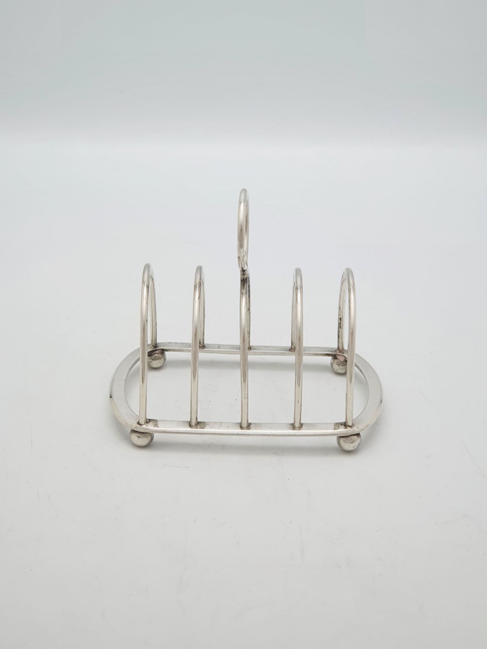 A small late Victorian sterling silver toast rack featuring five arched divisions, a central ring handle, and four ball feet. View II