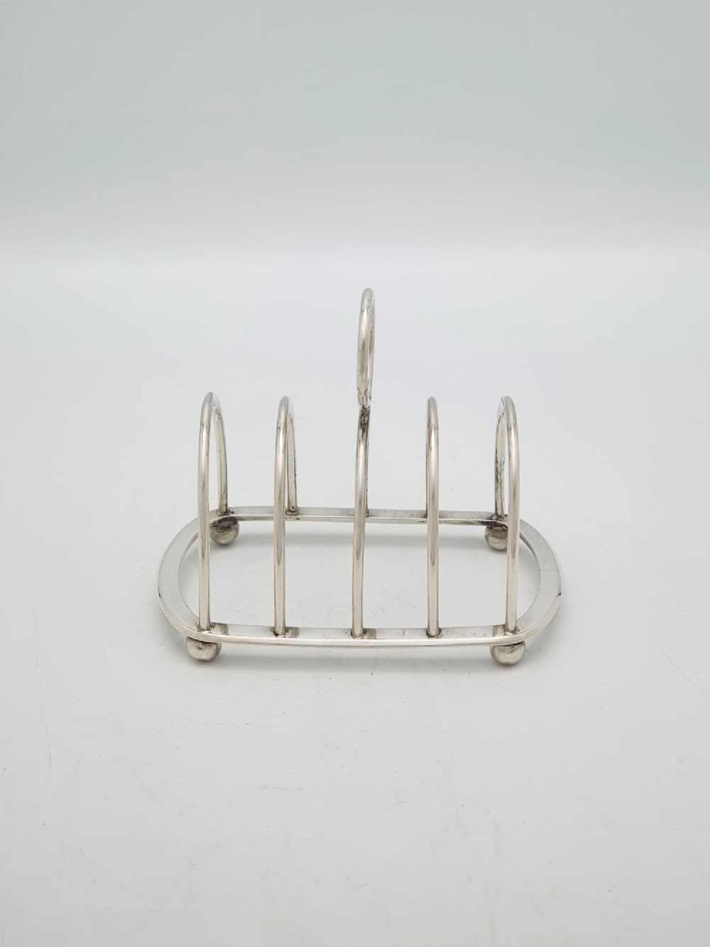 A small late Victorian sterling silver toast rack featuring five arched divisions, a central ring handle, and four ball feet. View IV