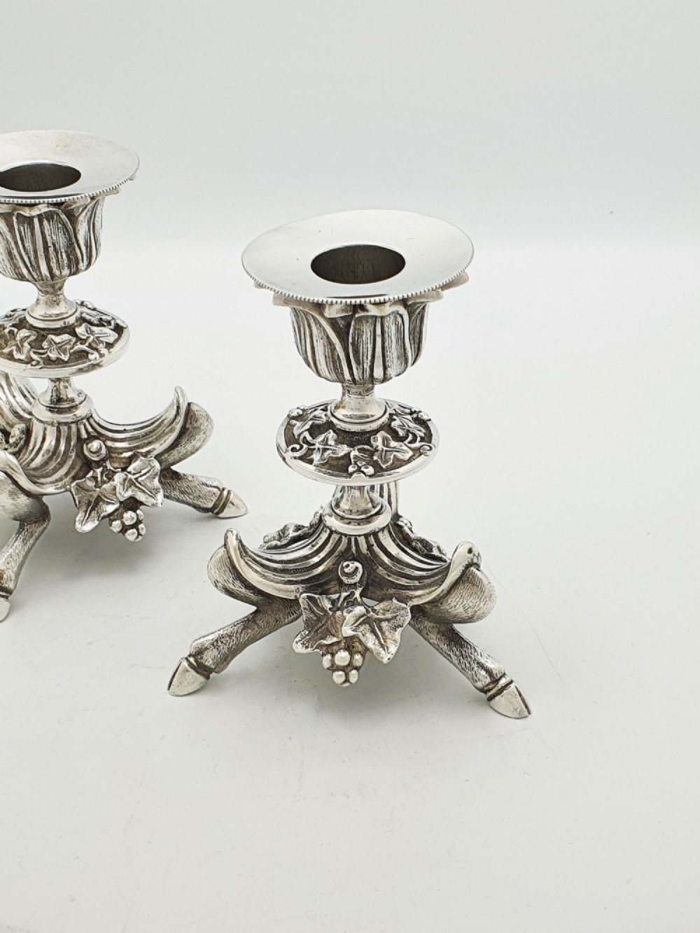 A pair of Victorian silver-plated candlesticks featuring fluted holders, grape leaf ornamentation, and tripod bases shaped like animal hooves. View II