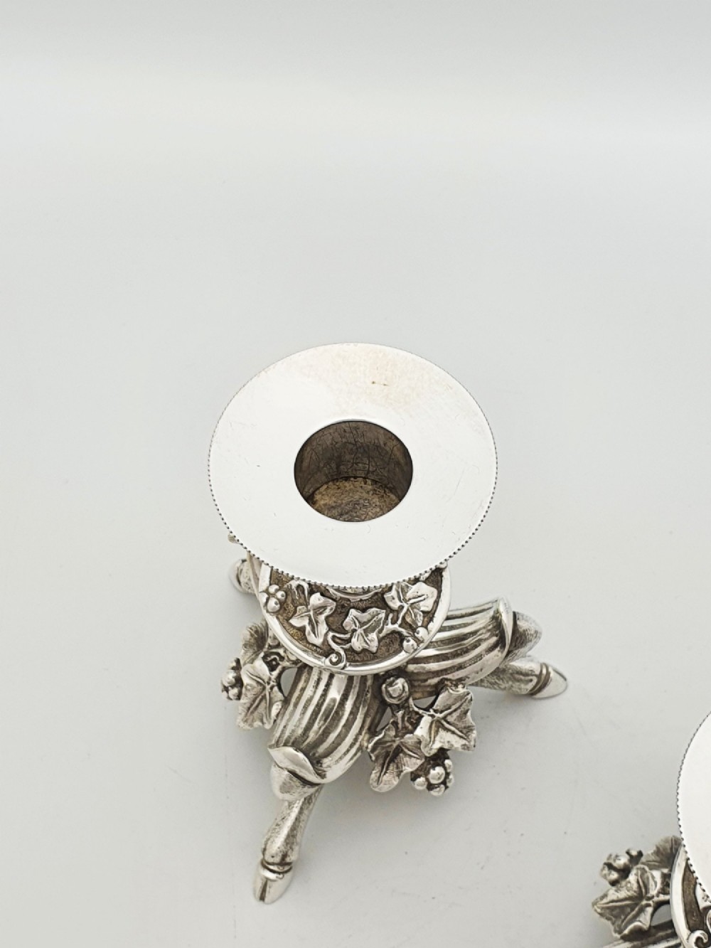 A pair of Victorian silver-plated candlesticks featuring fluted holders, grape leaf ornamentation, and tripod bases shaped like animal hooves. View V