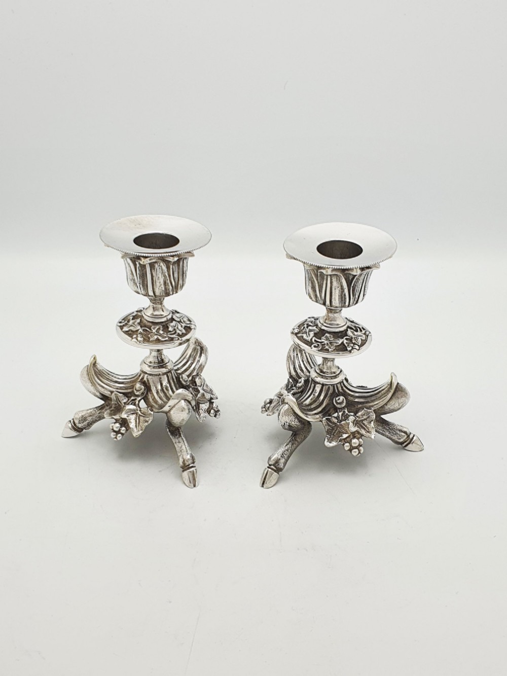 A pair of Victorian silver-plated candlesticks featuring fluted holders, grape leaf ornamentation, and tripod bases shaped like animal hooves. View VI