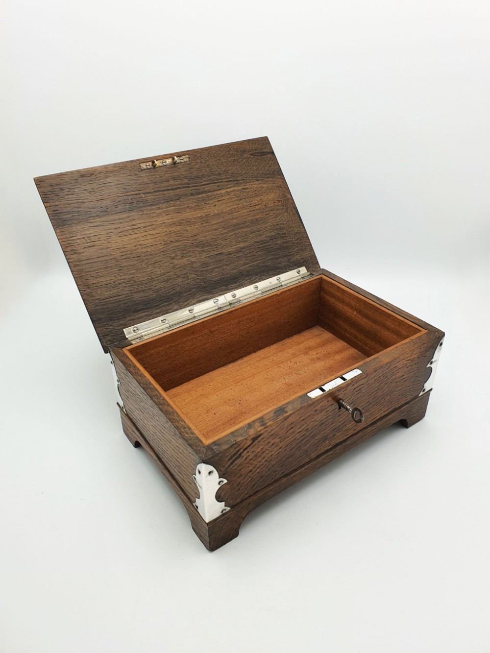An Edwardian oak cigar box featuring decorative sterling silver corner mounts, a central shaped silver plaque, and a front keyhole with key. View II