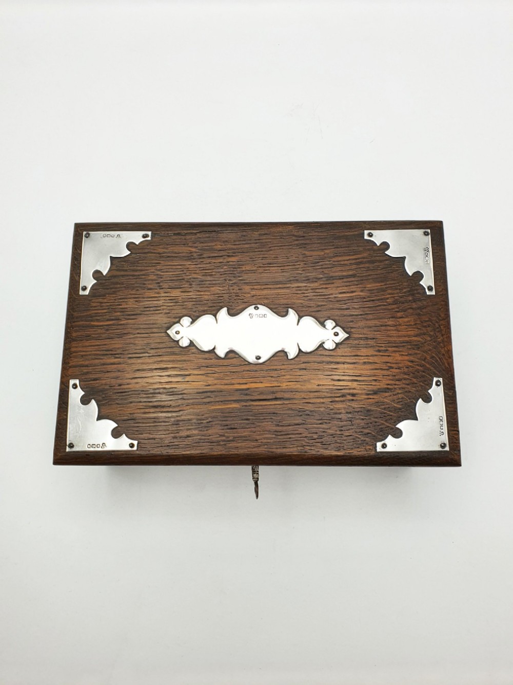 An Edwardian oak cigar box featuring decorative sterling silver corner mounts, a central shaped silver plaque, and a front keyhole with key. View VI