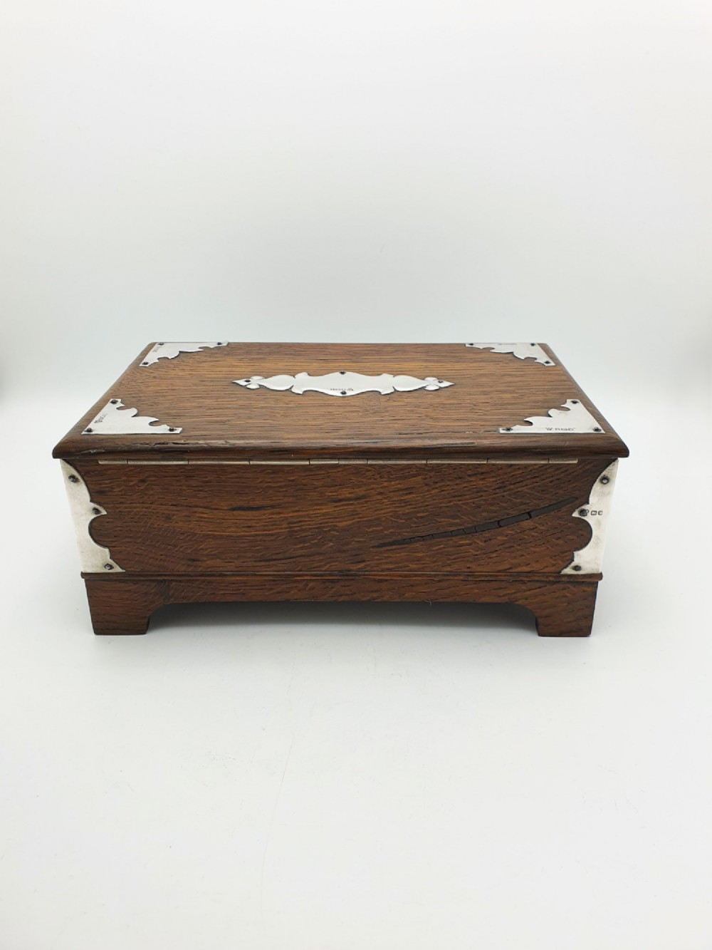 An Edwardian oak cigar box featuring decorative sterling silver corner mounts, a central shaped silver plaque, and a front keyhole with key. View X