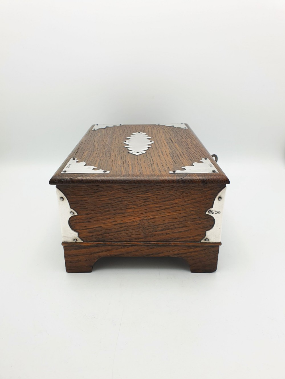 An Edwardian oak cigar box featuring decorative sterling silver corner mounts, a central shaped silver plaque, and a front keyhole with key. View XI