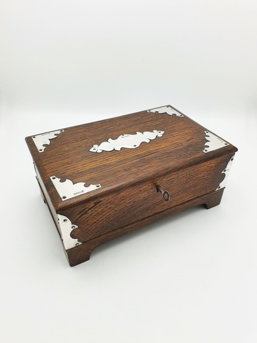 An Edwardian oak cigar box featuring decorative sterling silver corner mounts, a central shaped silver plaque, and a front keyhole with key. View XIII