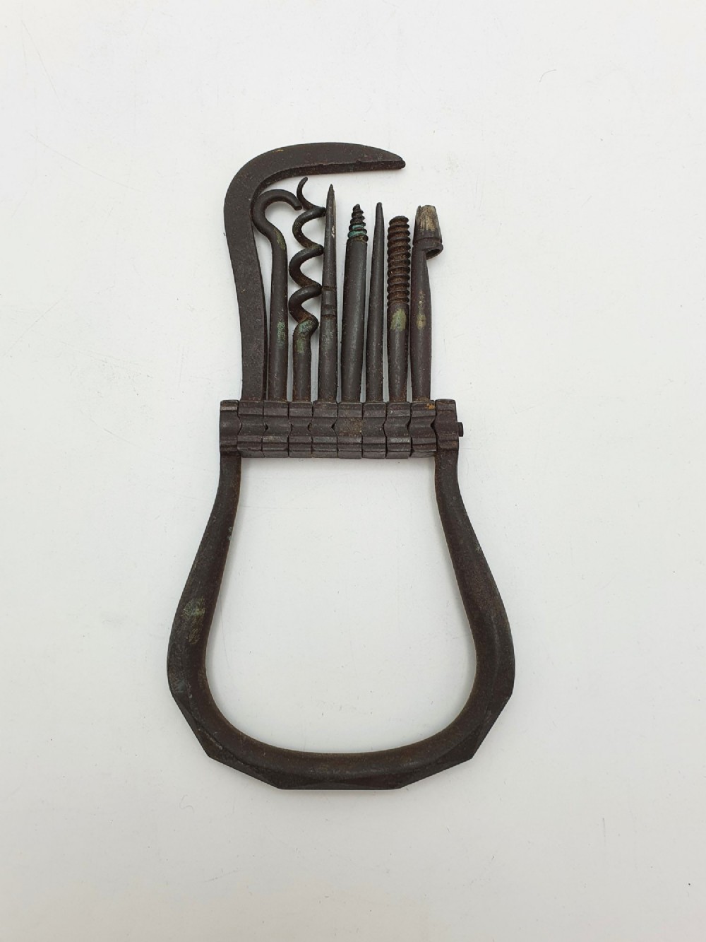 An antique Victorian dark iron folding multi-tool featuring multiple hinged implements including a corkscrew, gimlet, and spike set within a curved metal frame. View II