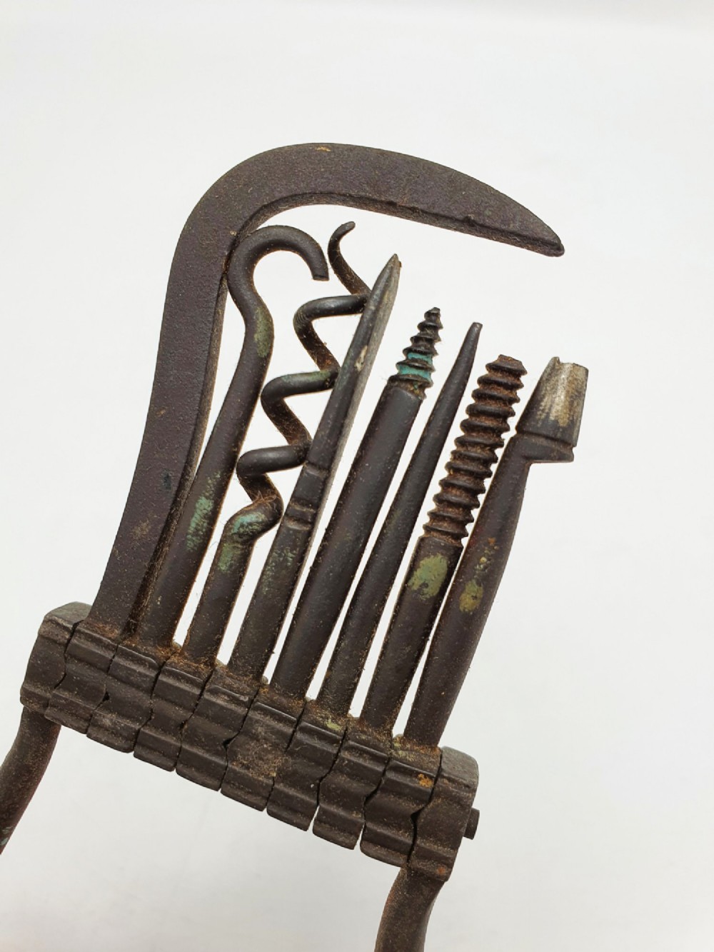 An antique Victorian dark iron folding multi-tool featuring multiple hinged implements including a corkscrew, gimlet, and spike set within a curved metal frame. View III