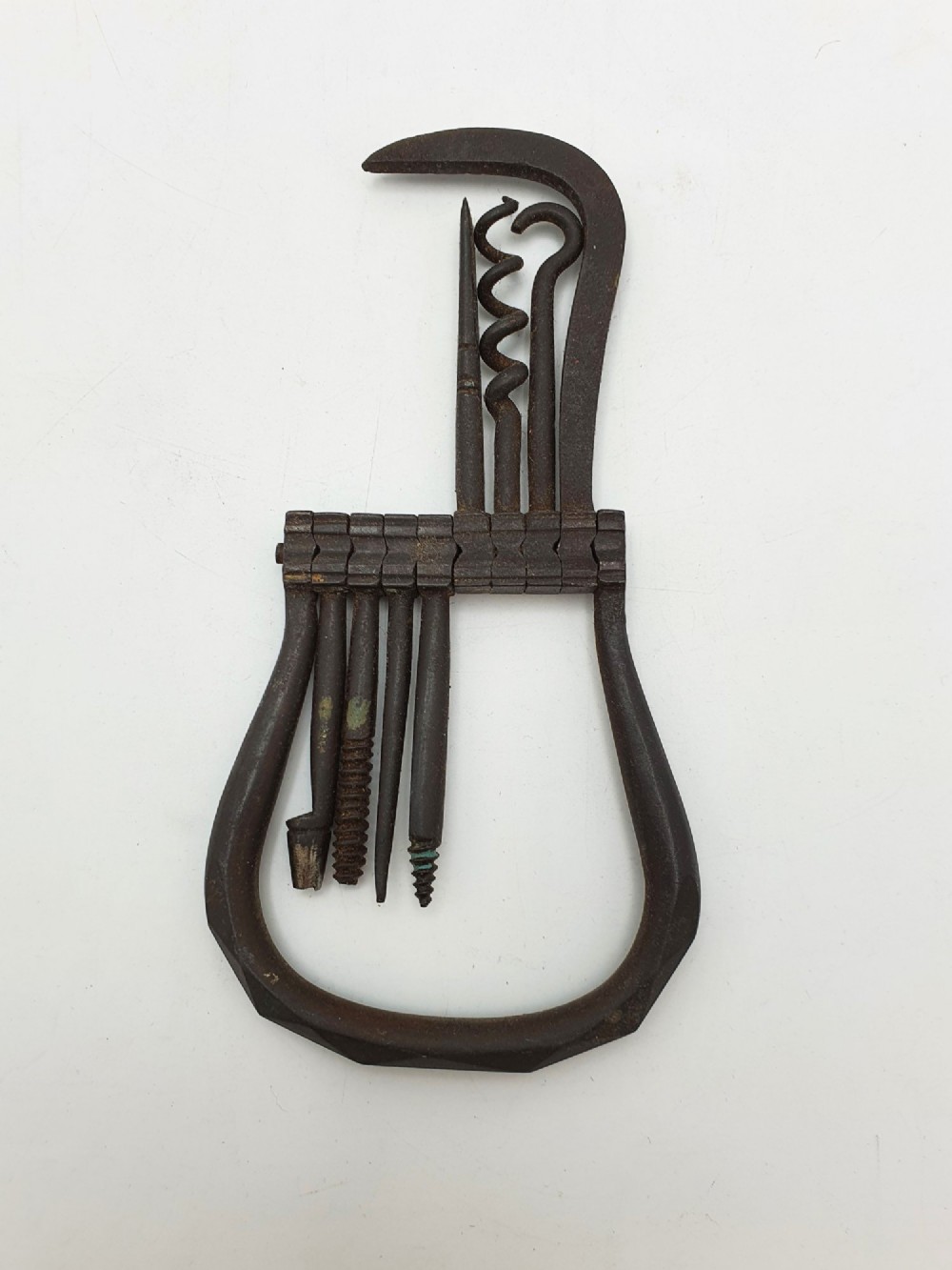 An antique Victorian dark iron folding multi-tool featuring multiple hinged implements including a corkscrew, gimlet, and spike set within a curved metal frame. View V