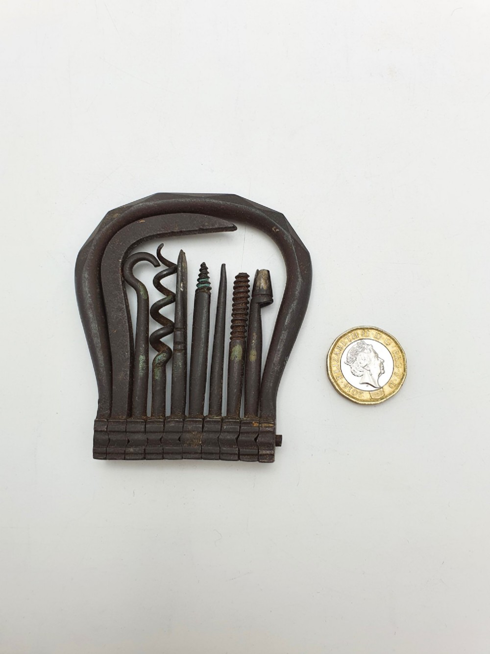An antique Victorian dark iron folding multi-tool featuring multiple hinged implements including a corkscrew, gimlet, and spike set within a curved metal frame. View VI
