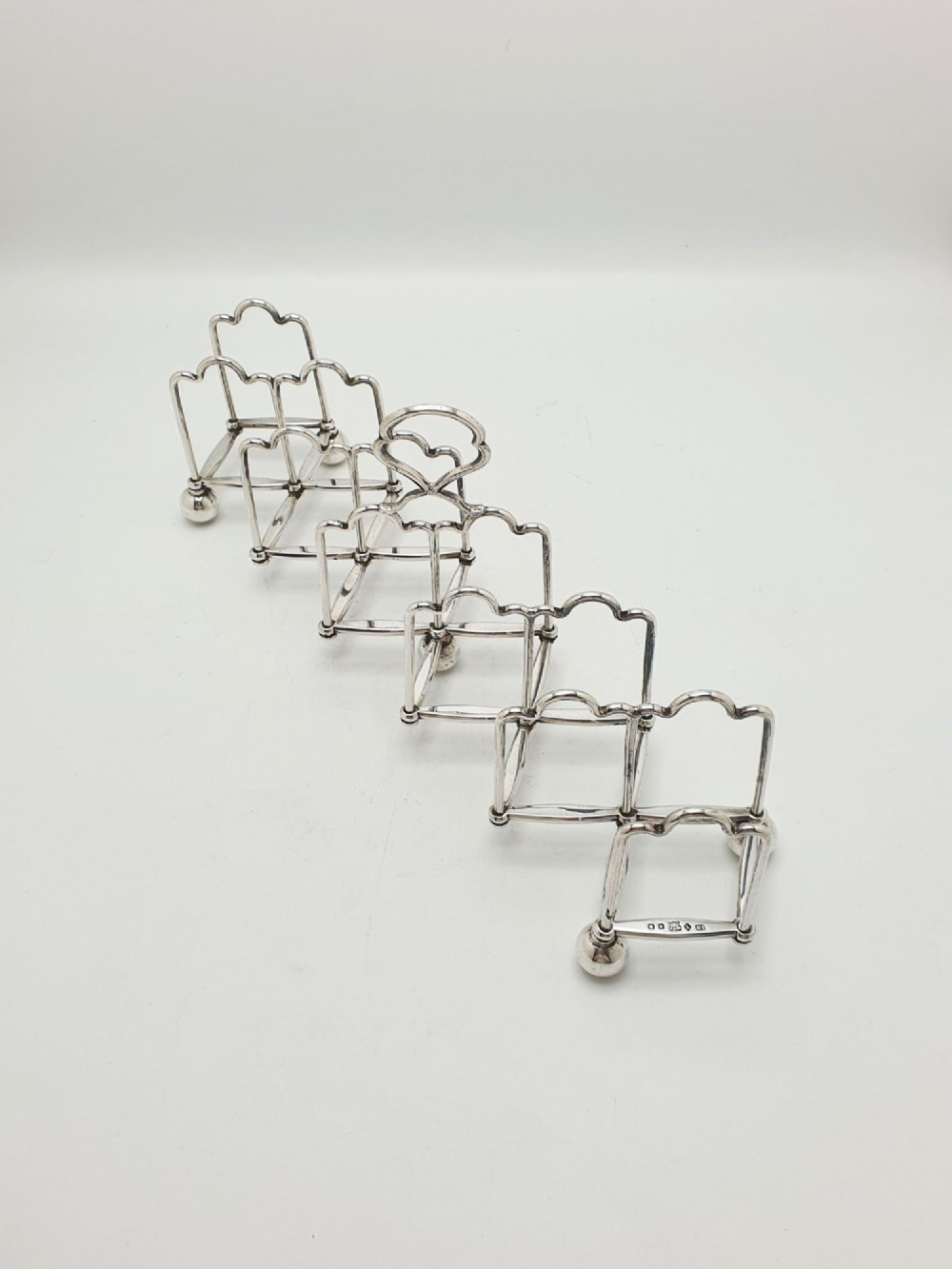 An antique silver-plated extending toast rack featuring an articulated concertina base, arched dividers, ball feet, and a central loop handle. View II
