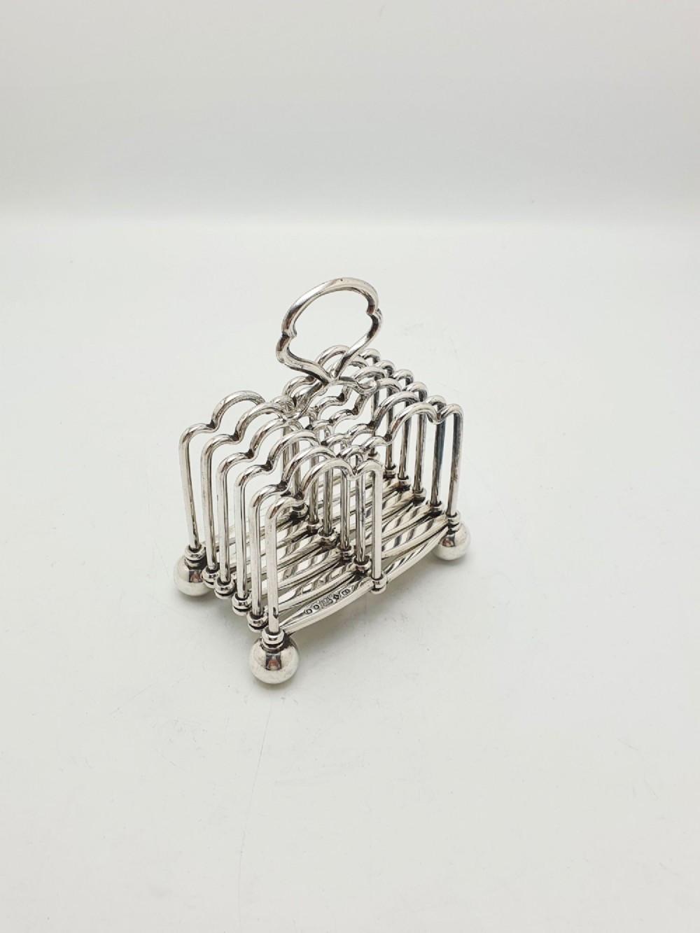 An antique silver-plated extending toast rack featuring an articulated concertina base, arched dividers, ball feet, and a central loop handle. View III