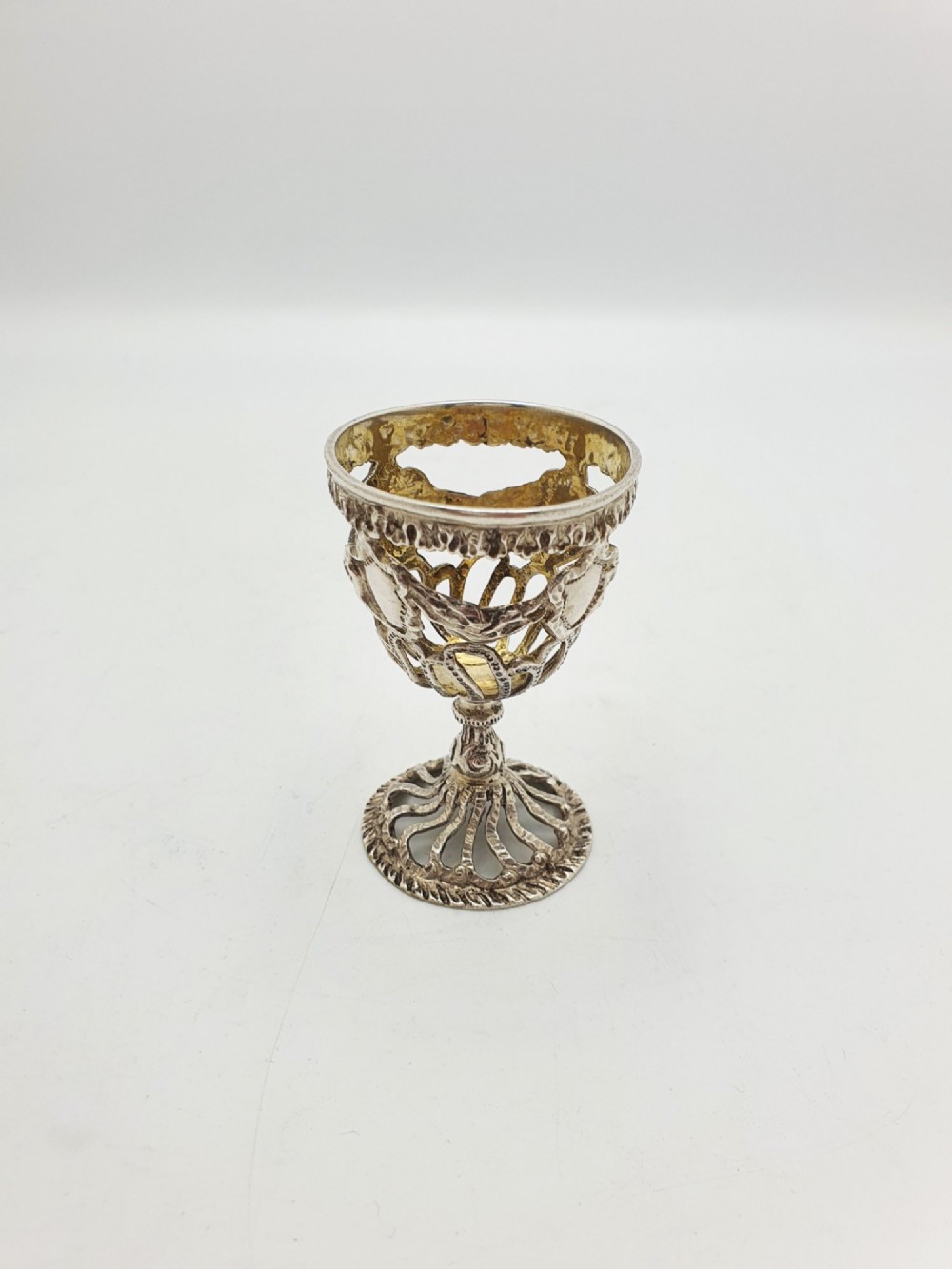 An Edwardian sterling silver egg cup featuring openwork lattice carving, a gilded interior wash, and a footed pedestal base.
