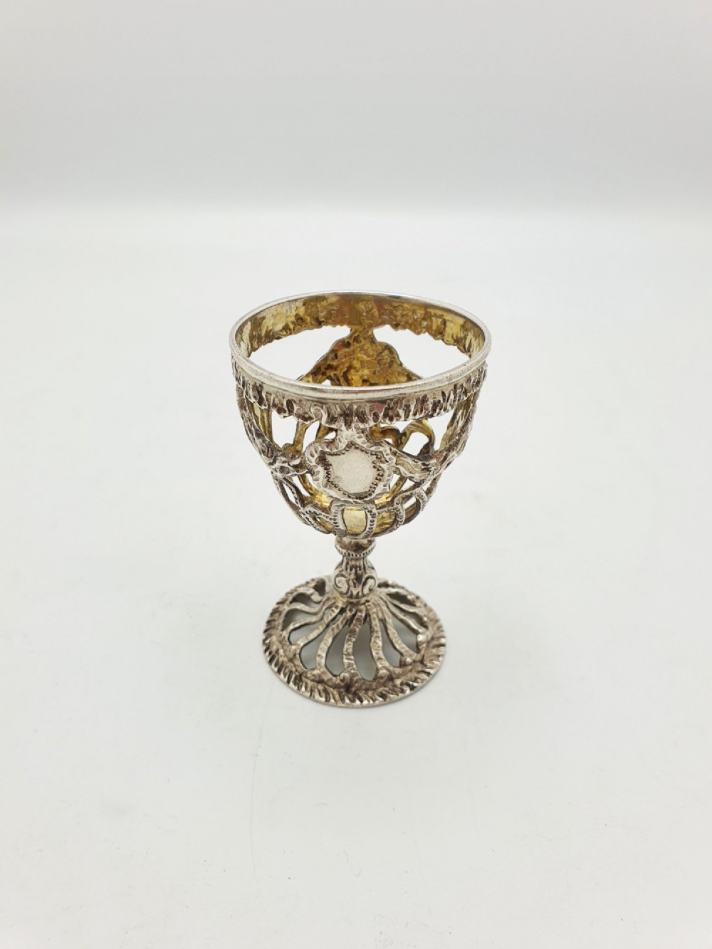 An Edwardian sterling silver egg cup featuring openwork lattice carving, a gilded interior wash, and a footed pedestal base. View II
