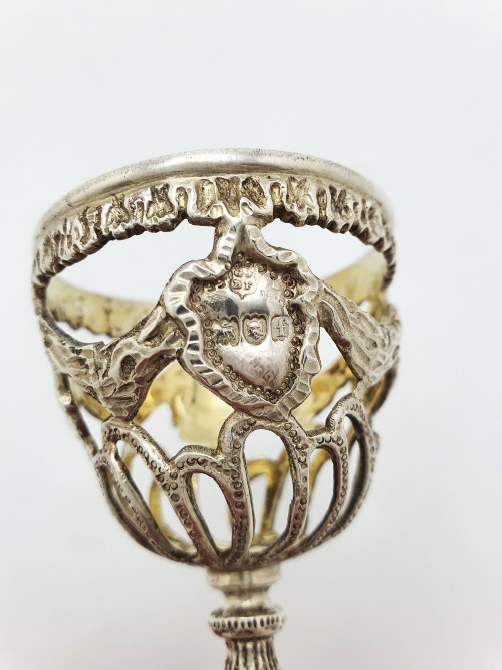 An Edwardian sterling silver egg cup featuring openwork lattice carving, a gilded interior wash, and a footed pedestal base. View V