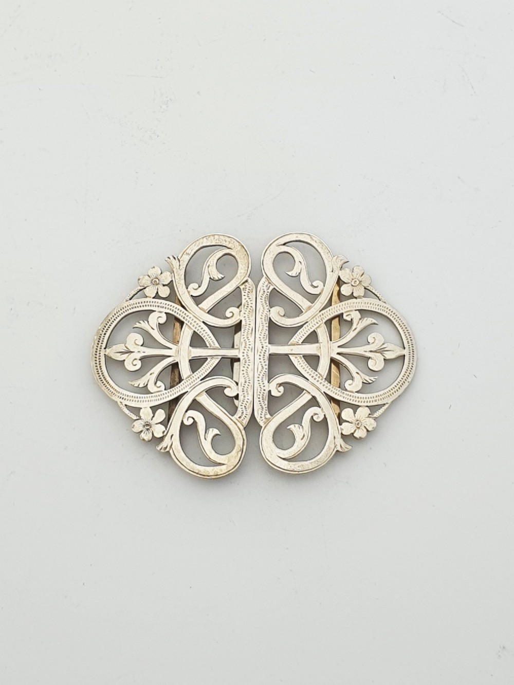 An Edwardian two-part sterling silver belt buckle featuring pierced scrollwork and floral motifs.