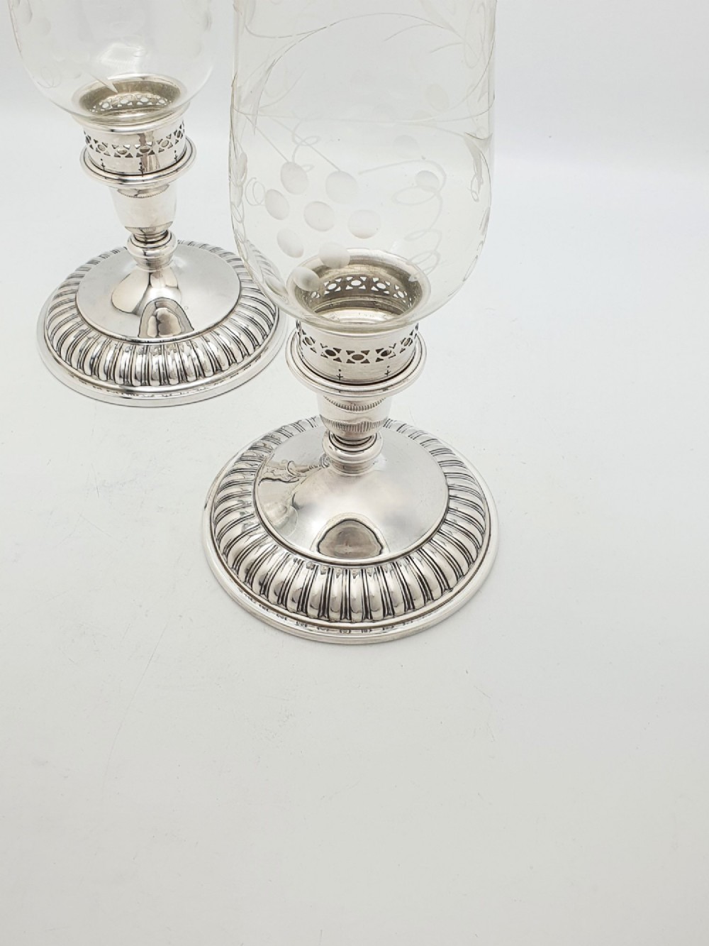 A pair of silver-plated candle holders featuring gadrooned bases and pierced sockets topped with etched glass hurricane shades. View III