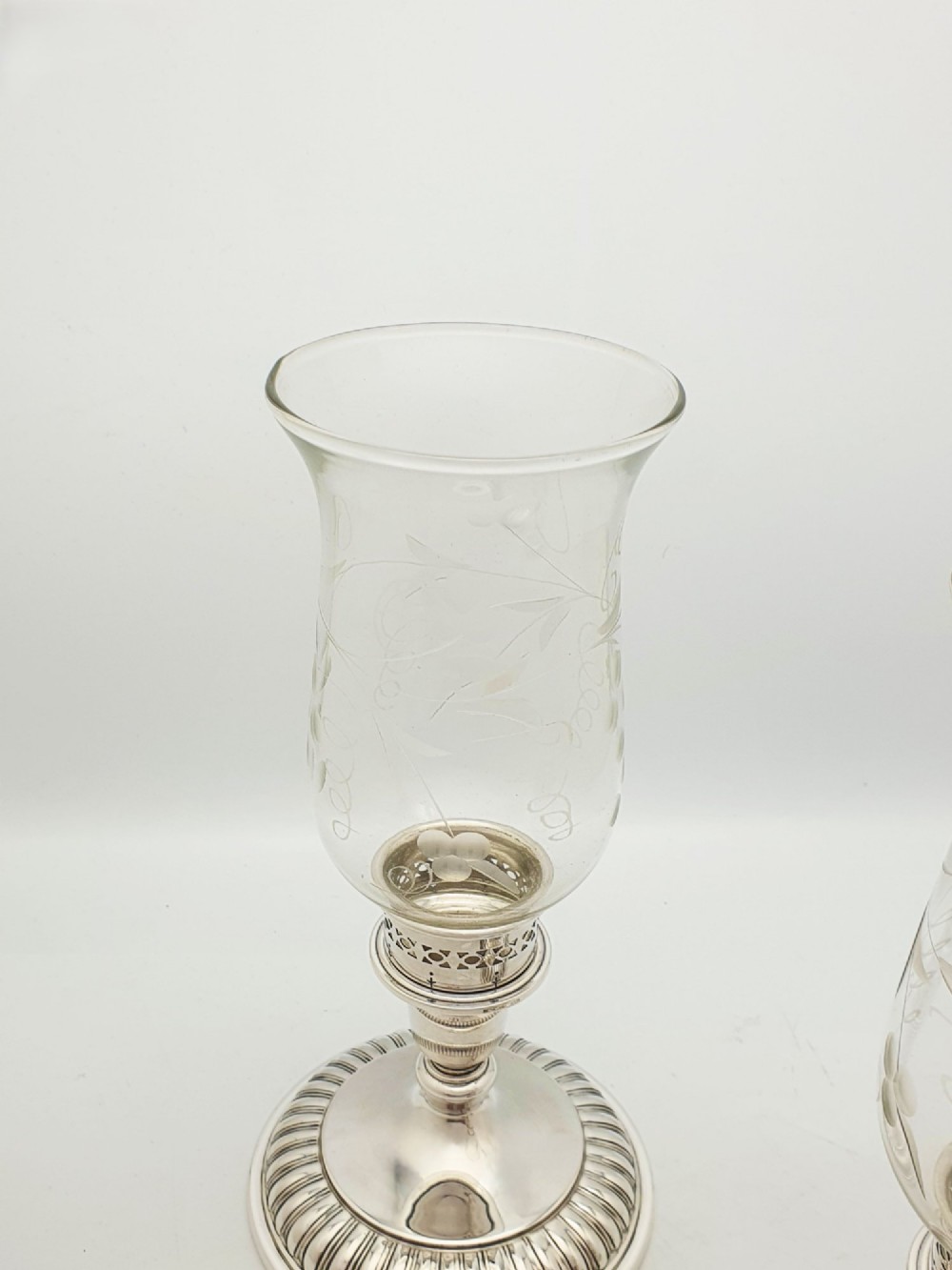 A pair of silver-plated candle holders featuring gadrooned bases and pierced sockets topped with etched glass hurricane shades. View IV