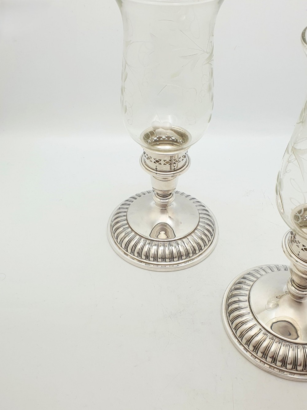A pair of silver-plated candle holders featuring gadrooned bases and pierced sockets topped with etched glass hurricane shades. View V