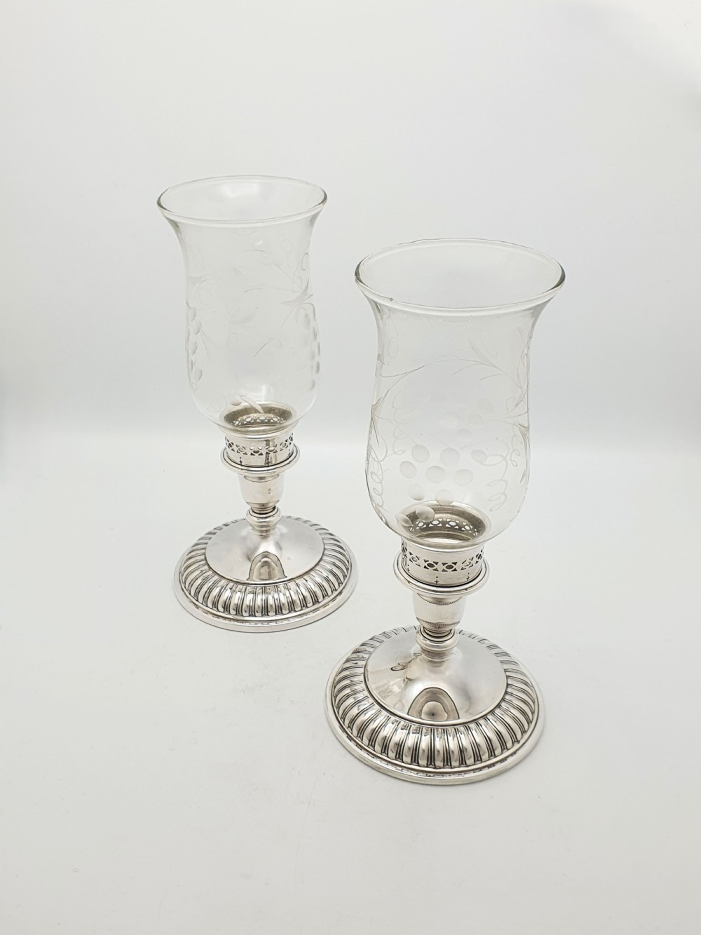 A pair of silver-plated candlestick bases fitted with clear etched glass hurricane shades featuring subtle floral patterns.
