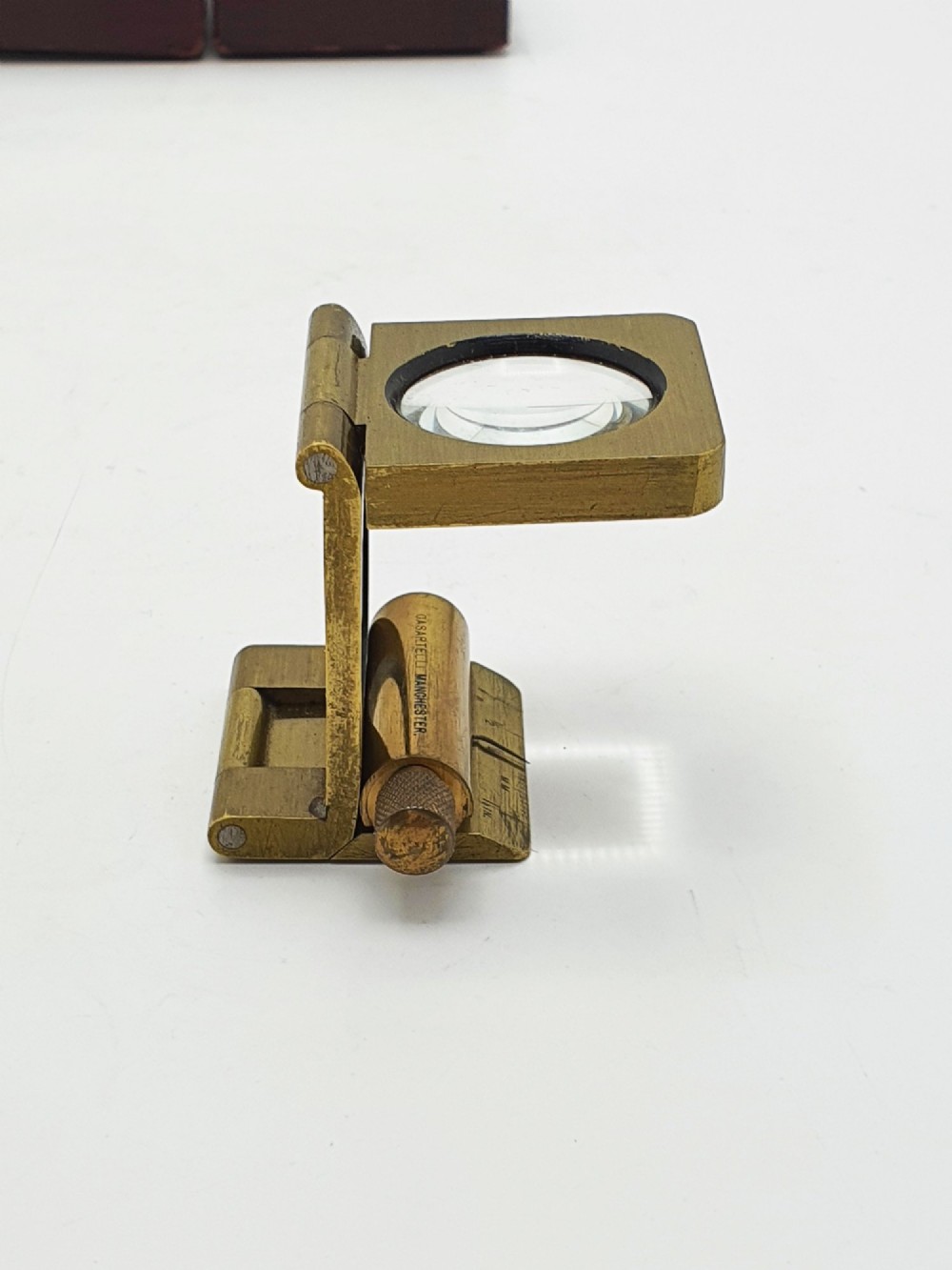 A vintage Edwardian folding brass linen tester loupe with a glass lens and measuring scale engraved on the base plate.