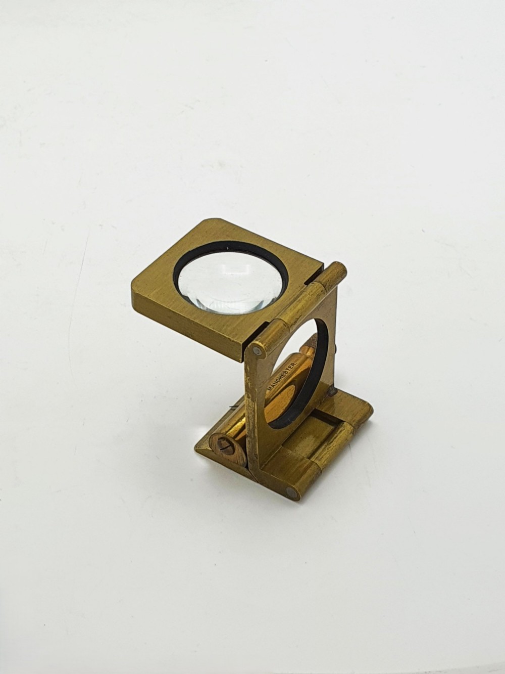 A vintage Edwardian folding brass linen tester loupe with a glass lens and measuring scale engraved on the base plate. View V