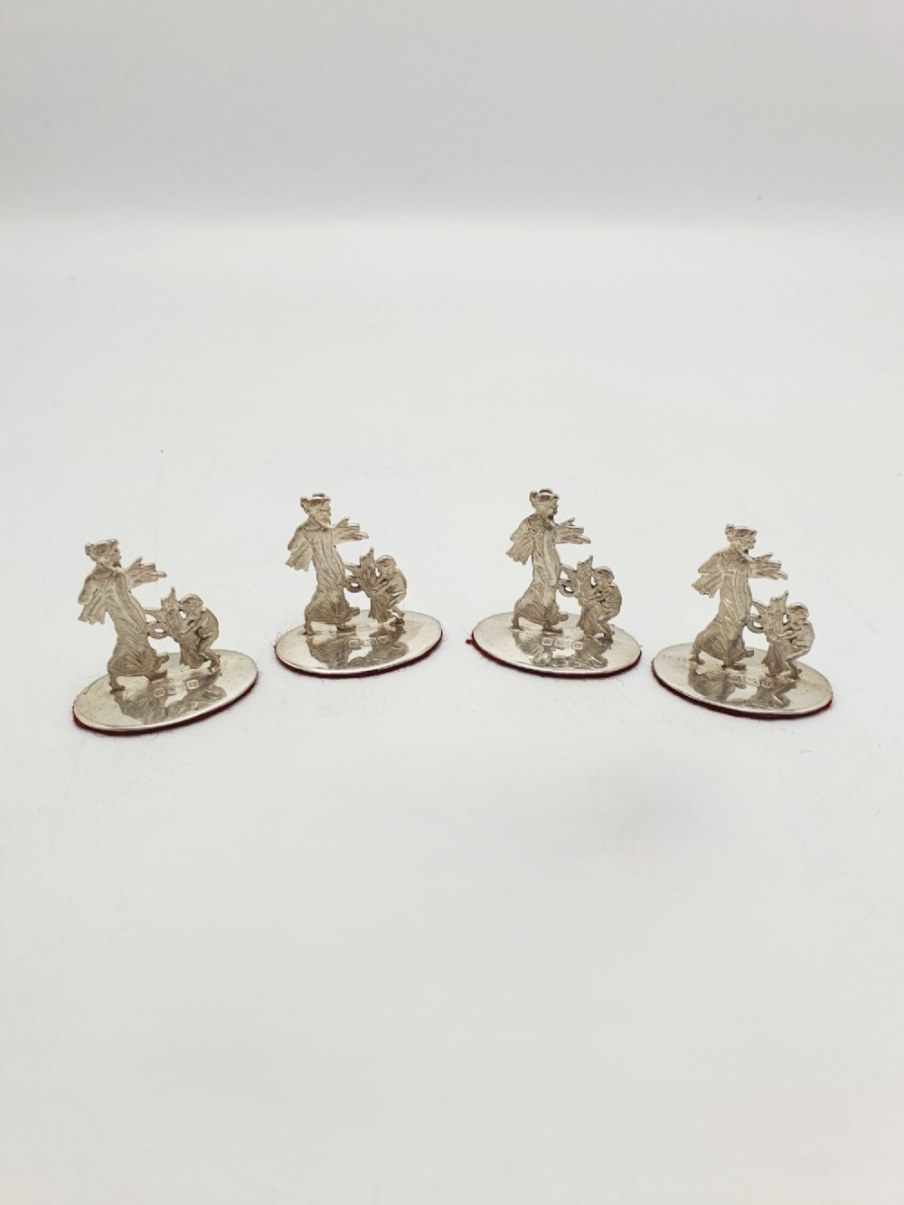 A set of four Edwardian sterling silver place card holders featuring figural motifs mounted on polished oval bases.