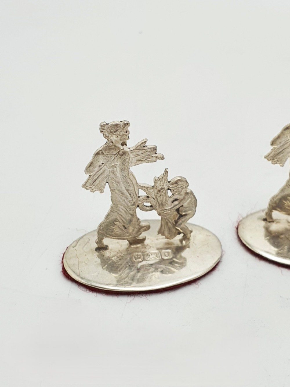 A set of four Edwardian sterling silver place card holders featuring figural motifs mounted on polished oval bases. View II