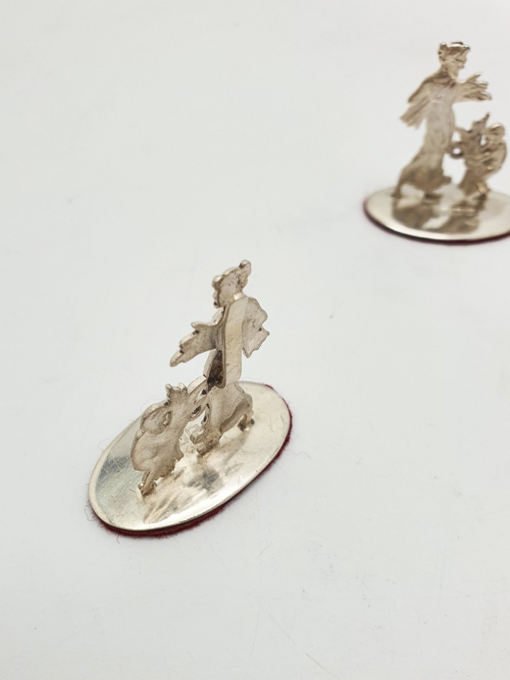 A set of four Edwardian sterling silver place card holders featuring figural motifs mounted on polished oval bases. View IV