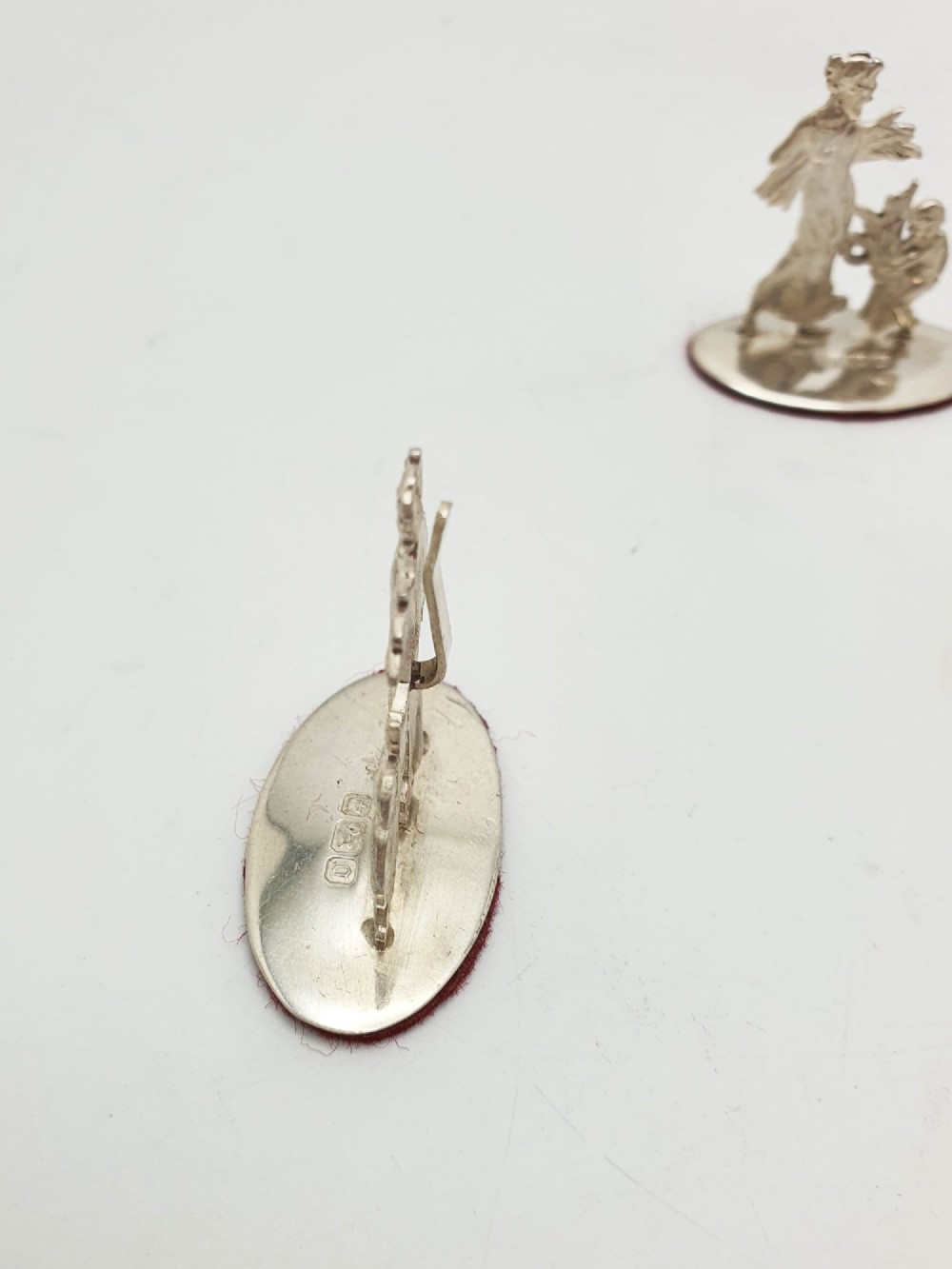 A set of four Edwardian sterling silver place card holders featuring figural motifs mounted on polished oval bases. View V