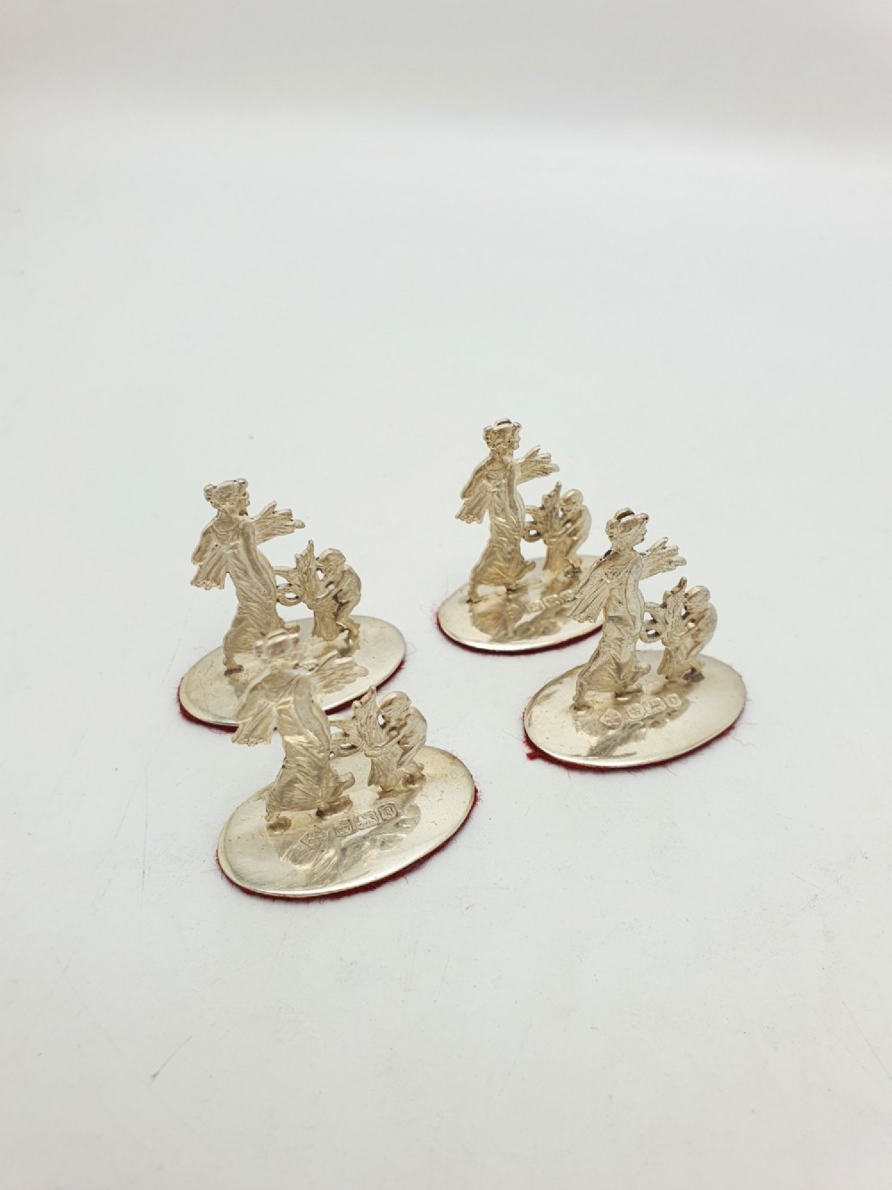 A set of four Edwardian sterling silver place card holders featuring figural motifs mounted on polished oval bases. View VI