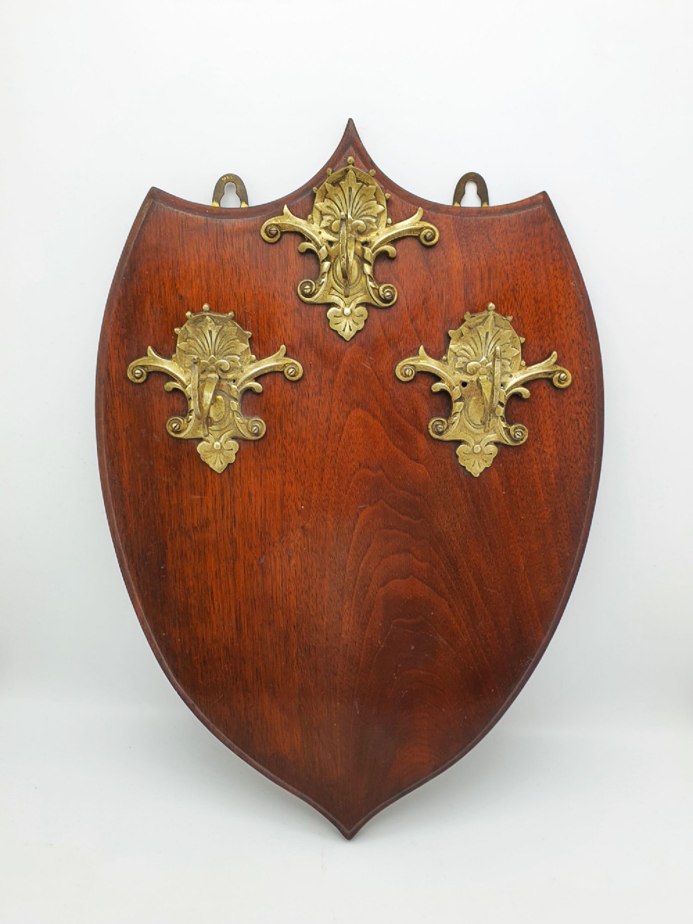 A shield-shaped mahogany wall plaque equipped with three decorative cast brass coat hooks arranged symmetrically. View II