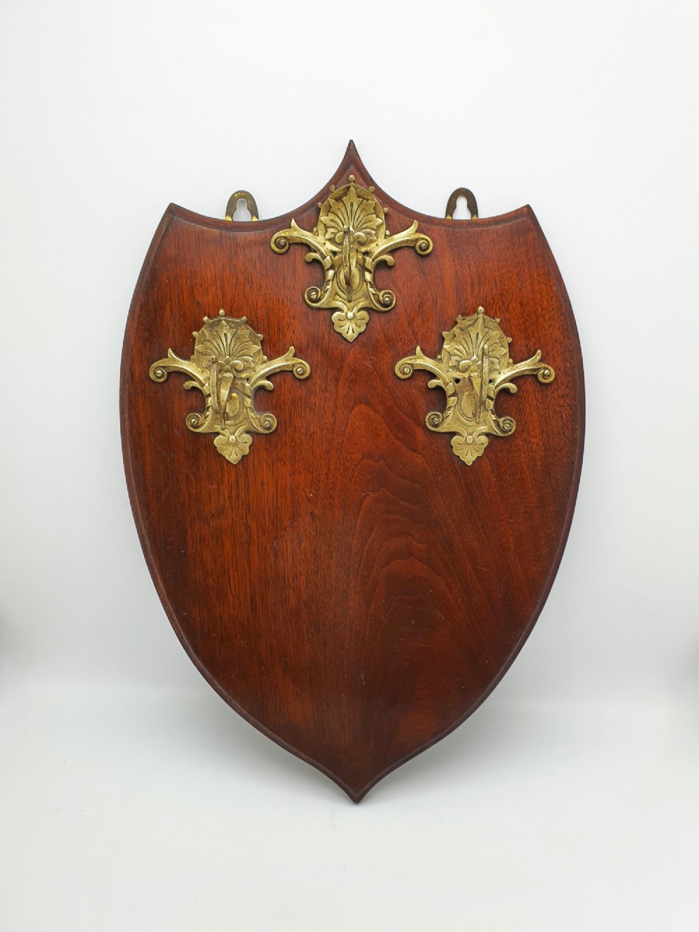 A shield-shaped mahogany wall plaque equipped with three decorative cast brass coat hooks arranged symmetrically. View III