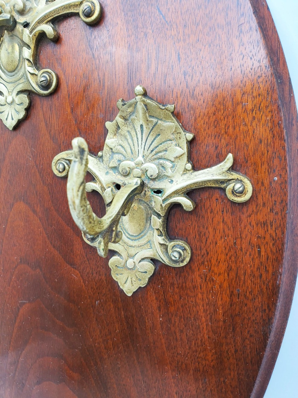 A shield-shaped mahogany wall plaque equipped with three decorative cast brass coat hooks arranged symmetrically. View VI